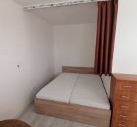 Hálószoba egy egyszobás lakásban ággyal, komóddal és fa dekorációjú padlóval.