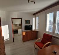 1 szobás lakás fa mintás padlóval, fotellel és konyhába vezető bejárattal.