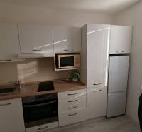 Konyha egy egyszobás lakásban, gépekkel és fehér bútorokkal.