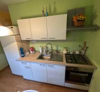 Konyha egy egyszobás lakásban fehér szekrényekkel és fa dekorációjú padlóval.