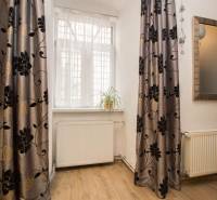 Szoba egy kétszobás lakásban, fa dekoros padlóval, függönyökkel és egy virággal a párkányon.