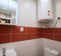 Fürdőszoba fehér bojlerrel, mosdóval és tükrös szekrénnyel egy kétszobás lakásban.