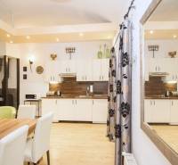 Két szobás lakás konyhája fa mintázatú padlóval, fehér szekrényekkel és asztallal.