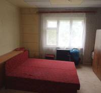 Hálószoba egy családi házban egyszerű bútorokkal és piros ággyal.