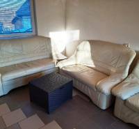 Bézs kanapé a házikóban rattan asztallal, napfény az ablakon keresztül.