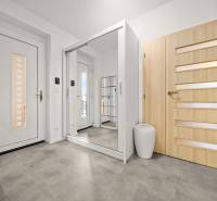 Előszoba fa mintázatú padlóval, tükrös szekrény és világos ajtók családi házban.