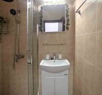 Fürdőszoba a nyaraló apartmanban zuhanyzóval és mosdóval, világos csempékkel burkolva.