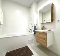 Háromszobás lakás fürdőszobája káddal és fa dekorációjú bútorokkal.