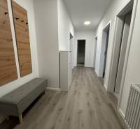 Folyosó egy háromszobás lakásban, világos falakkal és fa dekorációjú padlóval.