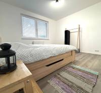 Hálószoba egy háromszobás lakásban, fa dekor padlóval, ággyal és éjjeliszekrénnyel.