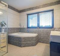 Fürdőszoba családi házban káddal, zuhanyzóval és mosdóval, világos csempékkel, redőnyös ablakkal.