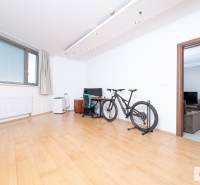 Szoba egy háromszobás lakásban, kerékpárral, íróasztallal és fa dekorációjú padlóval.