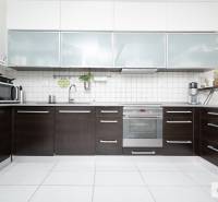 Konyha egy háromszobás lakásban, sötét konyhabútorral és fehér csempékkel.