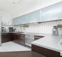 Konyha egy háromszobás lakásban fehér csempékkel és sötét szekrényekkel.