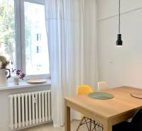 Lámpa a faasztal fölött, fehér függönyök és virágdekoráció az ablakpárkányon egy kétszobás lakásban.