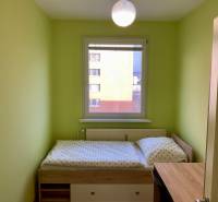 Szoba egy háromszobás lakásban zöld falakkal, ággyal és ablakkal.