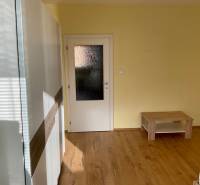 Szoba fa dekor padlóval, világos falakkal és egyszerű bútorokkal egy 3 szobás lakásban.