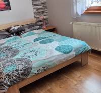 Hálószoba családi házban ággyal, radiátorral és fa dekorációjú padlóval.