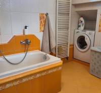 Fürdőszoba családi házban káddal, mosdóval, mosógéppel és sárga csempével.