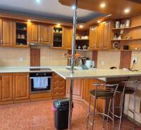 Konyha családi házban fa dekorációval, felszerelve háztartási gépekkel és bárpulttal.