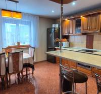 Konyha étkezőasztallal családi házban, fa szekrények és csempézett padló.