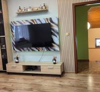 Nappali egy családi házban fa dekor padlóval és nagy televízióval a falon.