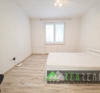 Világos hálószoba egy háromszobás lakásban, fa dekorációjú padlóval és egyszerű bútorokkal.