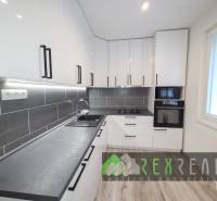 Konyha egy háromszobás lakásban fehér szekrényekkel és fa mintázatú padlóval.