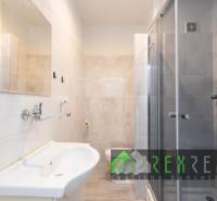 Háromszobás lakás fürdőszobája zuhanyzóval, mosdóval és világos csempékkel.