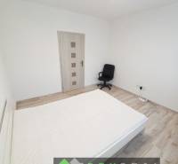 Világos hálószoba egy háromszobás lakásban, fa dekor padlóval és irodai székkel.