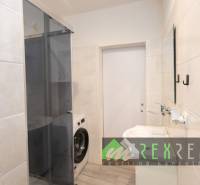 Fürdőszoba egy háromszobás lakásban zuhanyzóval és mosógéppel, csempézett falakkal.