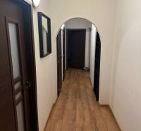 Keskeny folyosó egy kétszobás lakásban, fa mintázatú padlóval és sötét ajtókkal.