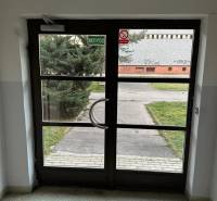 Üveg bejárati ajtó belülről, a kijárat egy gondozott gyephez és járdához vezet.