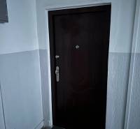 Bejárati ajtó egy kétszobás lakásban fehér falakkal és barna szőnyeggel.