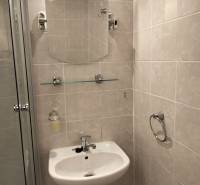 Fürdőszoba mosdóval, tükörrel és zuhanyzóval egy kétszobás lakásban.