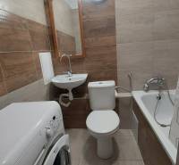 Fürdőszoba egy egyszobás lakásban káddal, mosdóval és mosógéppel, kerámia csempével burkolva.