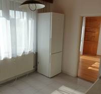 Konyha függönnyel és hűtőszekrénnyel egy egyszobás lakásban, fa mintázatú padlóval.