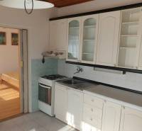 Konyha egy egyszobás lakásban fehér szekrényekkel, tűzhellyel és fa dekoros padlóval.