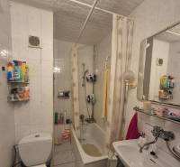 Fürdőszoba fehér csempékkel, káddal és mosdóval egy egyszobás lakásban.