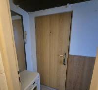 Előszoba egy egyszobás lakásban mosógéppel, ajtókkal és csempézett padlóval.