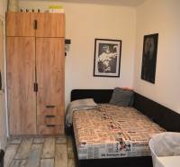 Szoba egy háromszobás lakásban, ággyal, szekrénnyel és fa dekorációjú padlóval.