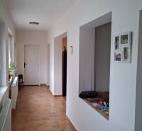 Családi ház folyosója csempével és fehér falakkal, a jobb oldalon nyitott ajtókkal.