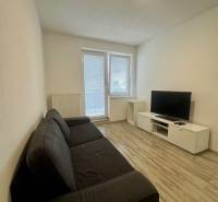 Nappali egy kétszobás lakásban kanapéval, televízióval és fa mintázatú padlóval.