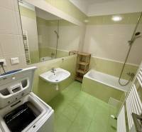 Fürdőszoba egy kétszobás lakásban káddal, mosdóval és felültöltős mosógéppel.