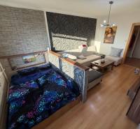 Nappali kanapéval, ággyal és fa dekorációjú padlóval egy háromszobás lakásban.