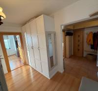 Folyosó egy 3 szobás lakásban, fa dekoros padlóval, fehér szekrényekkel és tükörrel.