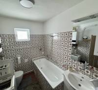 Fürdőszoba családi házban csempézett falakkal, káddal és mosógéppel.