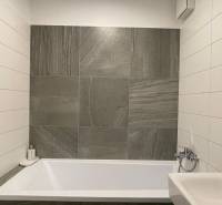 Fürdőszoba modern csempével és káddal egy kétszobás lakásban.