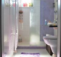 Fürdőszoba egy egyszobás lakásban WC-vel, mosdóval és ablakkal. A világos csempék dominálnak.