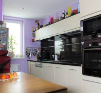 Konyha egy egyszobás lakásban világos szekrénnyel, székkel és gyümölcsökkel az asztalon.